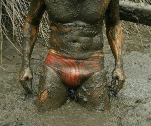 muddy man in red, latex briefs, standing in the swamp