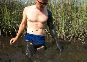 man in square cut speedo swimsuit, sanding in mud up to thighs