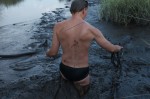 man crotch deep in swamp mud wearing black briefs