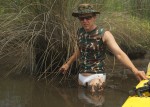 man in white bikini and camo top, up to crotch in swamp mud