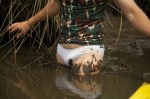man in white bikini and camo top, up to crotch in swamp mud, close up