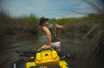 man in white bikini and camo top, pulling kayak in swamp
