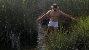 man in white cutoffs, walking in the swamp