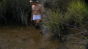 a man, wearing white cut-offs and walking in swamp mud