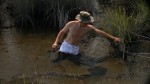 a man in swamp mud up to his crotch, wearing white cutoffs